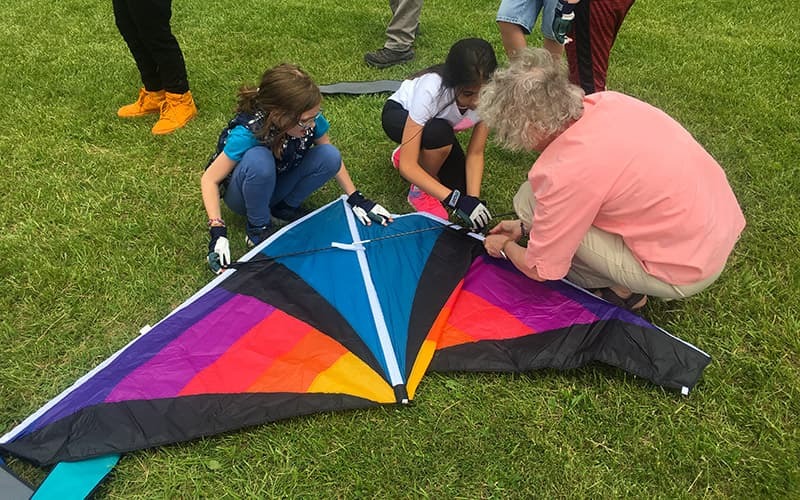 An educator working with two students on their kite before a takeoff.
