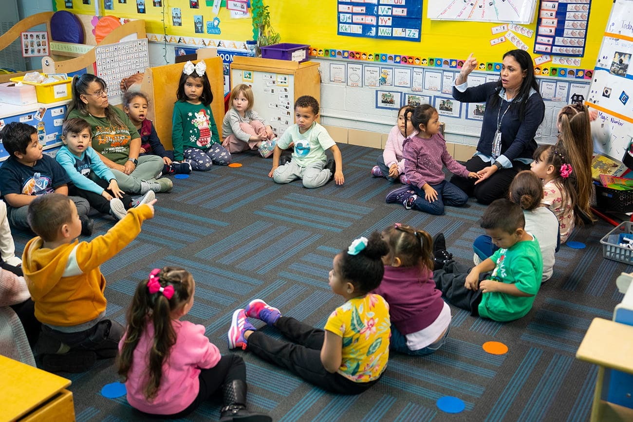 Group of stuents sitting in a circle with a teacher calling on students